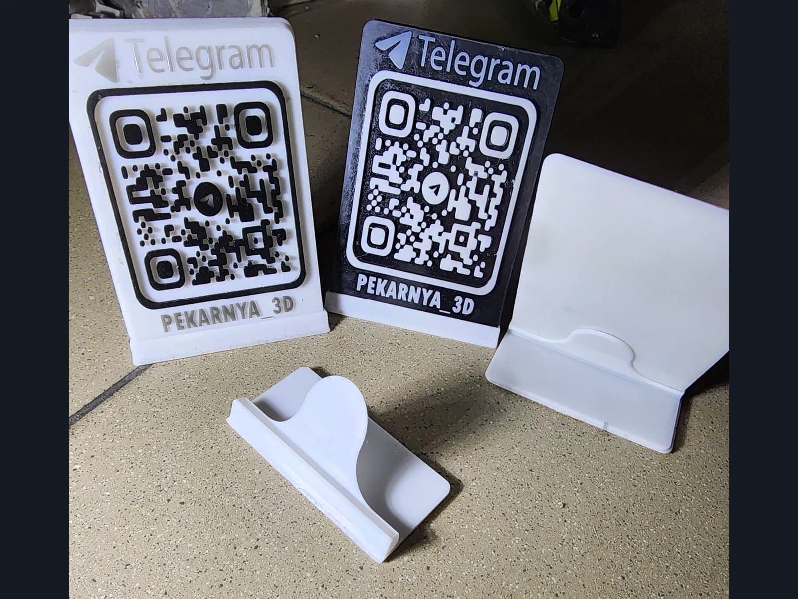 Светлая и тёмная QR-таблички с надписью Telegram, белая панель и отдельная подставка на рабочей поверхности.