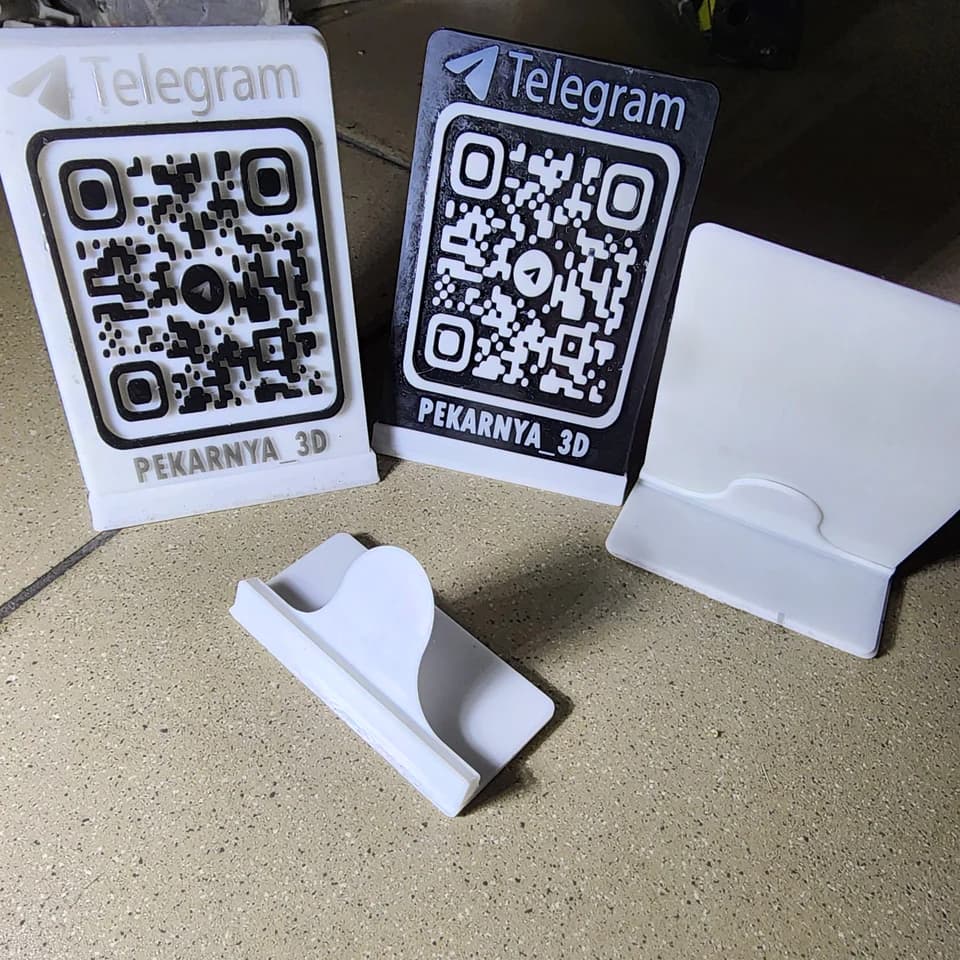Светлая и тёмная QR-таблички с надписью Telegram, белая панель и отдельная подставка на рабочей поверхности.